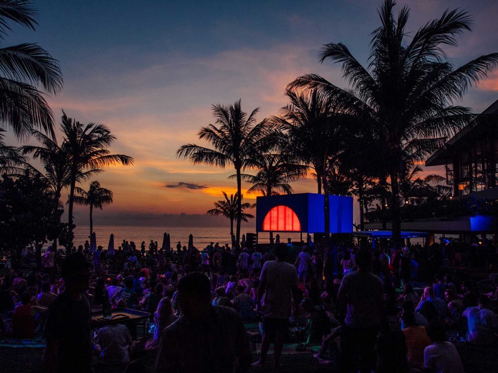 A crowd viewing a beautiful sunset amongst coconut trees at the Potato Head Beach Club located in Seminyak, Bali.