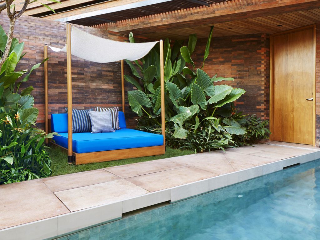 A blue day bed surrounded by lush greenery by the private pool at the Pool Suite at Potato Head Suites in Seminyak, Bali.