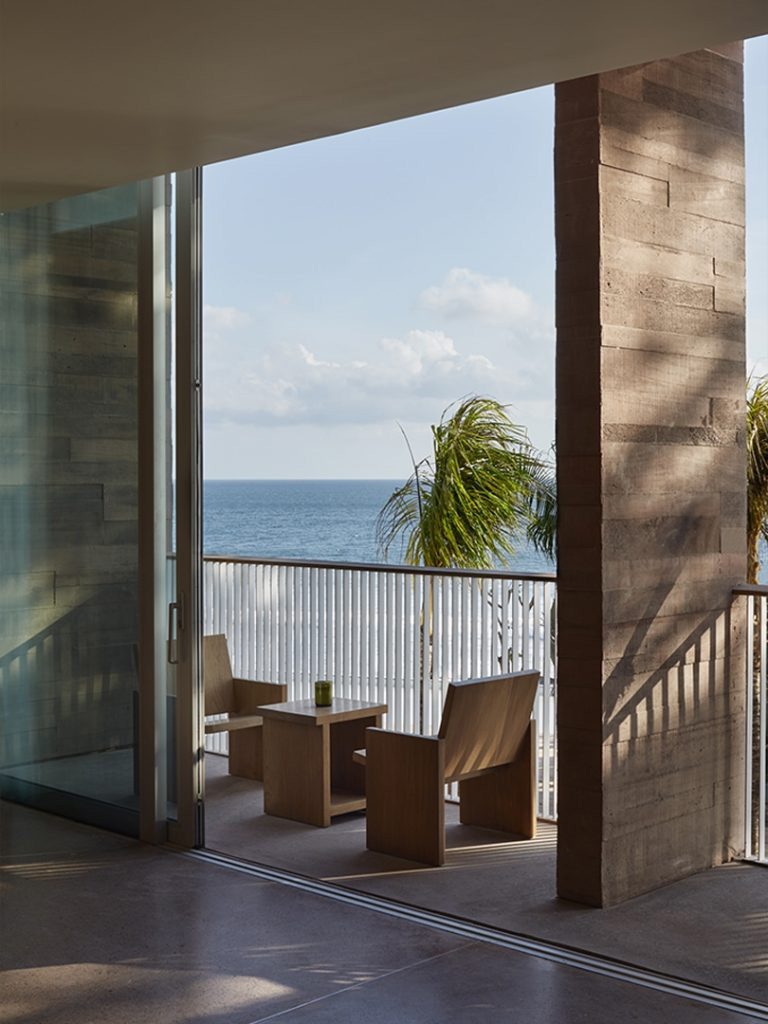 A wooden sitting area at the balcony of a studio at the Potato Head Studios in Seminyak features views of the ocean.