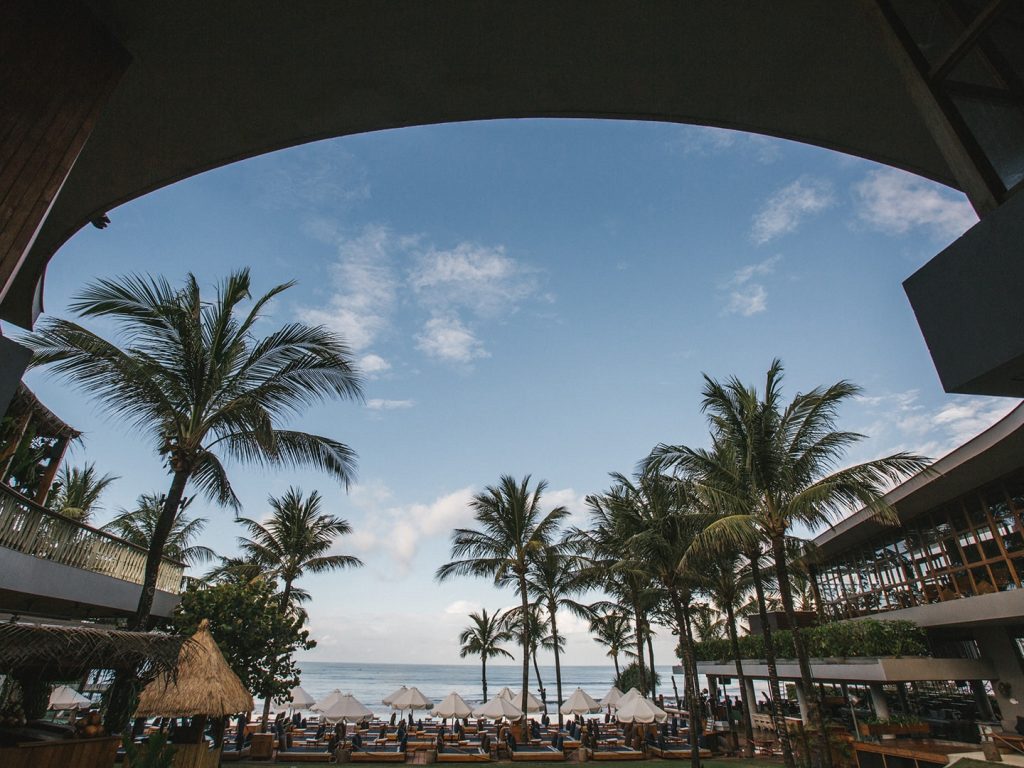 Day time view of Potato Head Beach Club, overlooking inviting daybeds, coconut trees and the ocean.
