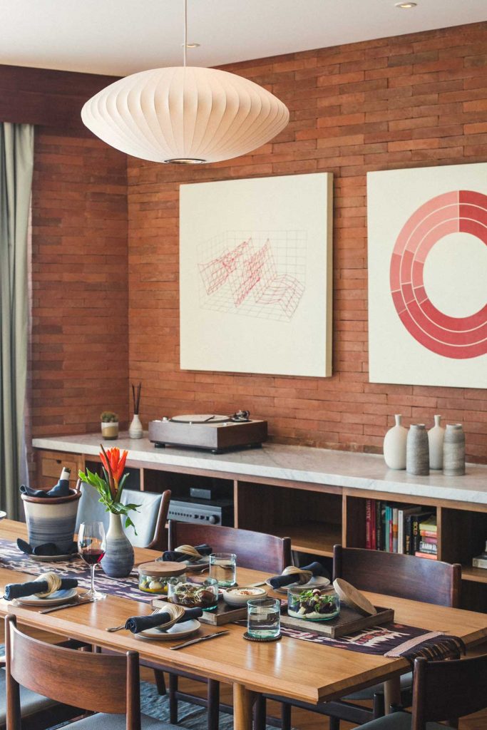 The dining area in the Potato Head Suites at Katamama Hotel features a long dining table, a vinyl player and wall art.