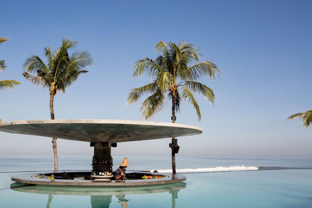 A bartender mixing drinks at a circular bar in the pool, overlooking the ocean at Potato Head Beach Club in Seminyak.