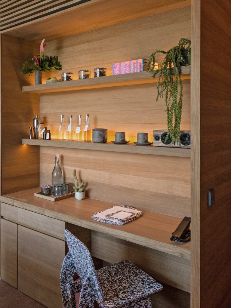 A wooden desk with shelves adorned with decorations, is paired with a Max Lamb chair at Potato Head Studios in Seminyak.
