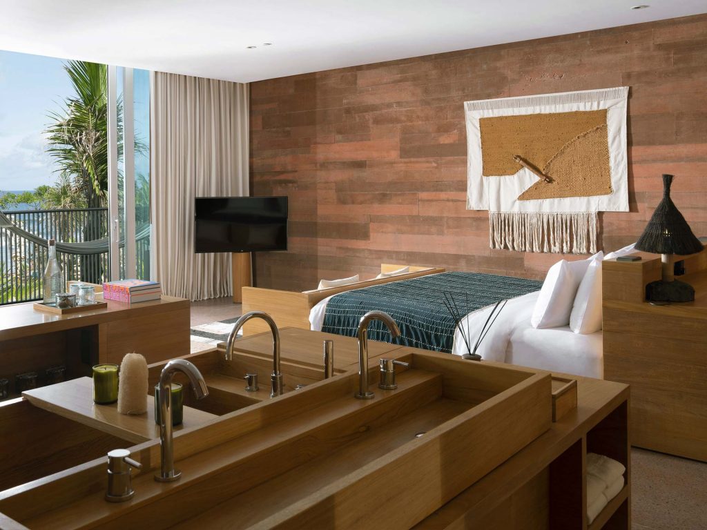 Part of the bathroom and the bedroom of the Oceanfront Studio, at Potato Head Studios in Seminyak, Bali, featuring a balcony.